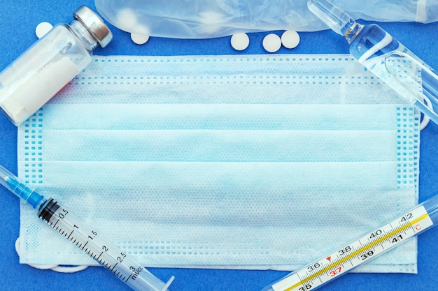 Medische beschermende maskers met thermometer, spuit, ampul, medicijnfles, pillen op blauw