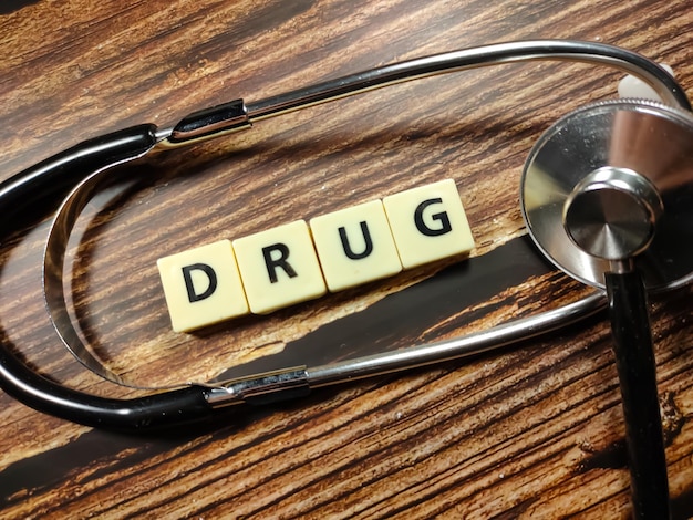 Foto medische concepttoys brief met woord drug en stethoscoop op houten achtergrond