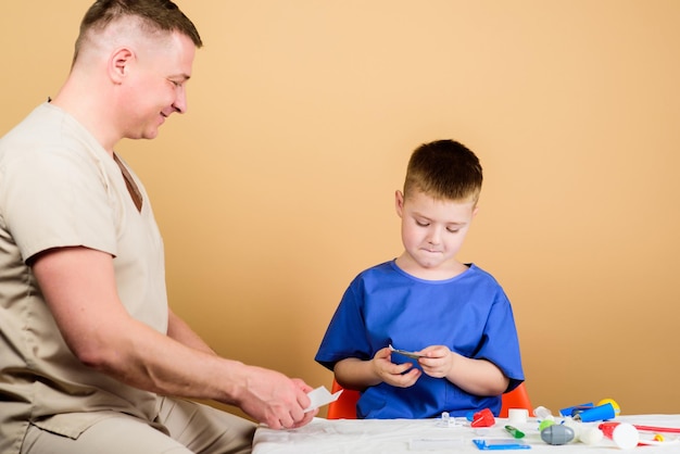 Medische hulp Medische verzekering Geneeskunde concept Kindje kleine dokter zitten aan tafel medische hulpmiddelen Gezondheidszorg Medisch onderzoek Salaris van ziekenhuismedewerker Jongen schattig kind en zijn vader arts