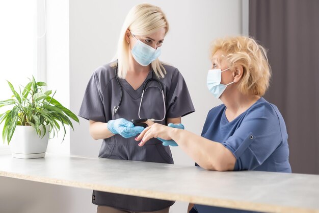 Medische hulp thuis. Vrouwelijke arts in een medisch masker meet de pols en zuurstofversadiging van de patiënt aan een vrouw van middelbare leeftijd met behulp van een pulsoximeter terwijl ze op de bank zit, gezondheidszorgconcept.