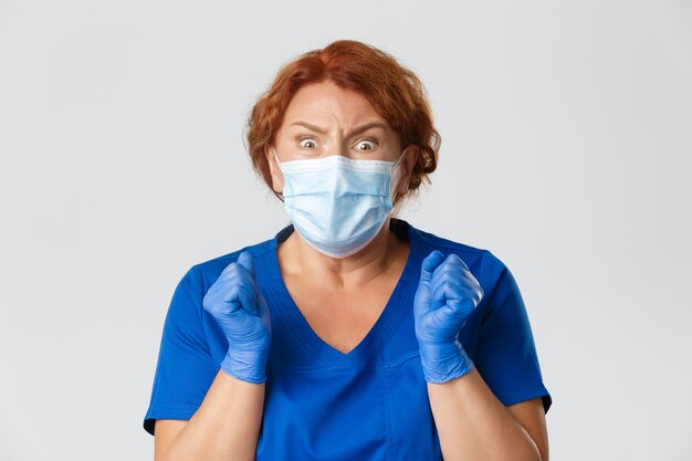 Medische hulpverleners, Covid-19 pandemie, coronavirus-concept. Close-up van bang vrouwelijke arts, verpleegster in gezichtsmasker en handschoenen schudden van angst en doodsbang kijken naar camera, grijze achtergrond.