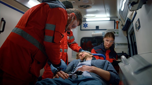 Foto medische hulpverleners zorgen voor slachtoffers op stretchers in een ambulance, multi-etnische paramedics meten de bloeddruk van de patiënt, medisch team onderzoekt de hartslag van de gewonde man.