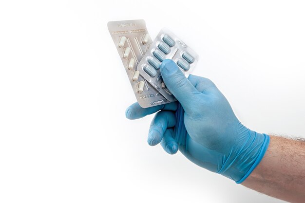 Medische latex of rubberhandschoenen blauw of blauw met tablet, geneeskunde, vitamine op de geïsoleerde mannelijke hand