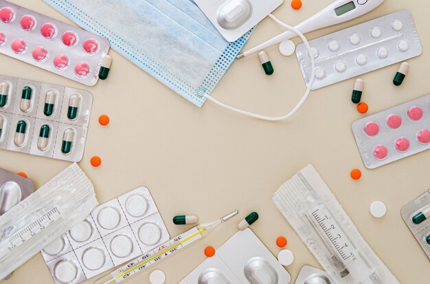 Medische masker, thermometer en medicijnen (pillen) op een beige achtergrond.