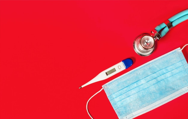 Medische masker thermometer en stethoscoop op een rode achtergrond Bovenbeeld kopieerruimte