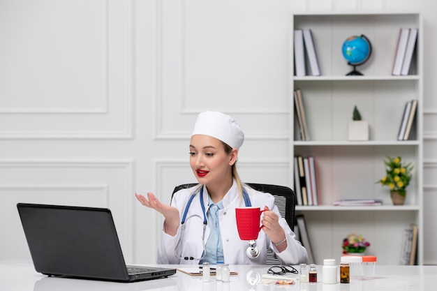 Medische mooie schattige dokter in witte laboratoriumjas en hoed met computer met rode kop