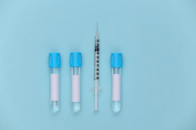 Medische reageerbuizen met spuit op blauwe pastelachtergrond. Vaccinatie. Bovenaanzicht