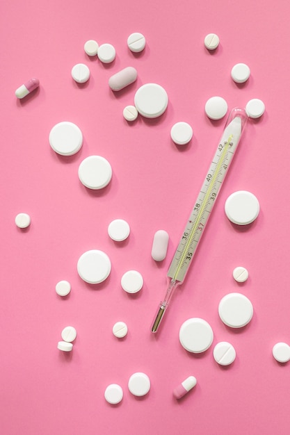 Medische thermometer en witte medicijnen of pillen op een roze achtergrond. Afslankproducten, vitamines, hormonen of kalmerende middelen. Gezondheidsconcept voor vrouwen.