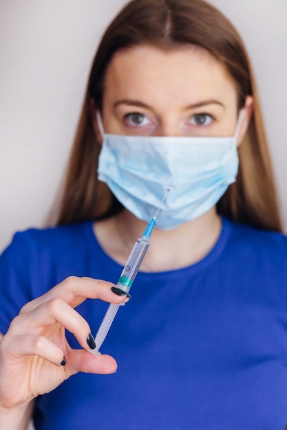 Medische werkneemster in een masker met een spuit, close-up hand met een spuit