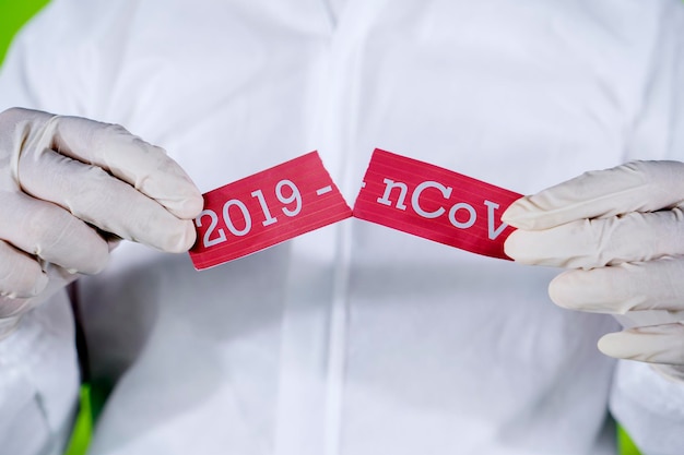 Medische werknemer handen scheuren tekst van 2019ncov op papier terwijl hij beschermende handschoenen en pak draagt Stop 2019nCoV of coronavirus concept