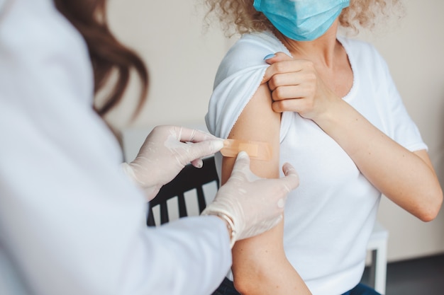 Medische zuster plakt een pleister op de arm van een jonge vrouw nadat ze haar het corona-virusvaccin tegen...