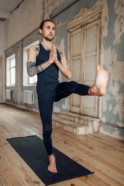 Meditatie in yogastudio, volledige concentratie. yoga met tatoeage evenwichtsoefening op mat in sportschool met grunge interieur.