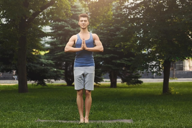 Meditating man with praying hands outdoors. Serene man practicing yoga and relaxing in park, copy space