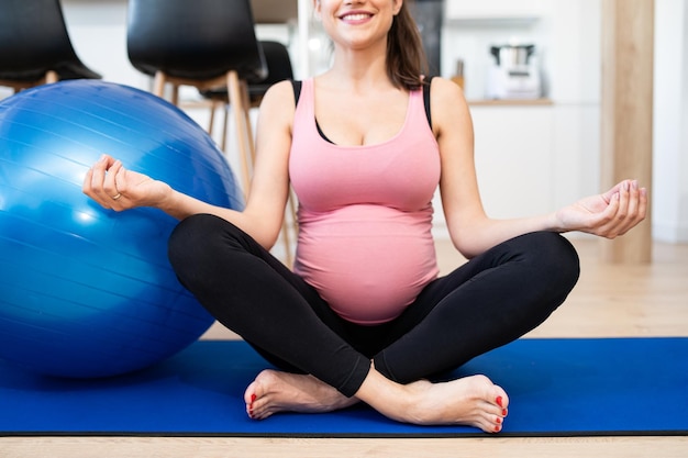 青いプロフェッシに座っているブルネットの髪を持つ妊婦の出産のクローズアップで瞑想