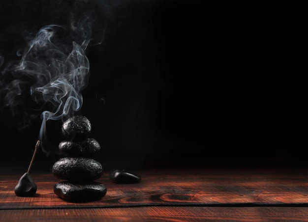 Meditation on Buddhist stones. Black stones with incense from a wooden table. Zen garden background