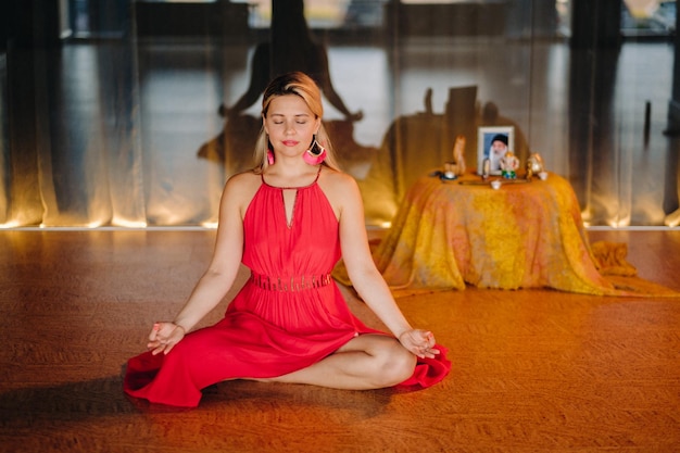瞑想と集中 目を閉じて床に座っている赤いドレスを着た女性が室内で薬を練習している 平和とリラクゼーション