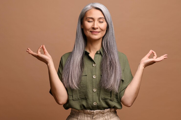 Photo meditation concept calm and satisfied mature woman holds her hands in zen gesture keeps eyes closed feels appeasement and pacification practicing yoga