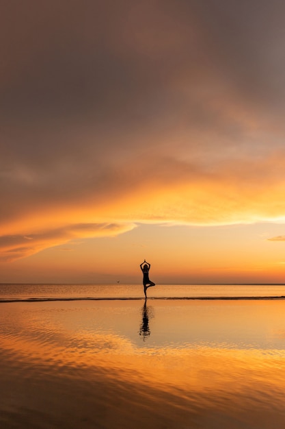 日没時にビーチでツリーヨガのポーズを練習する瞑想の女性