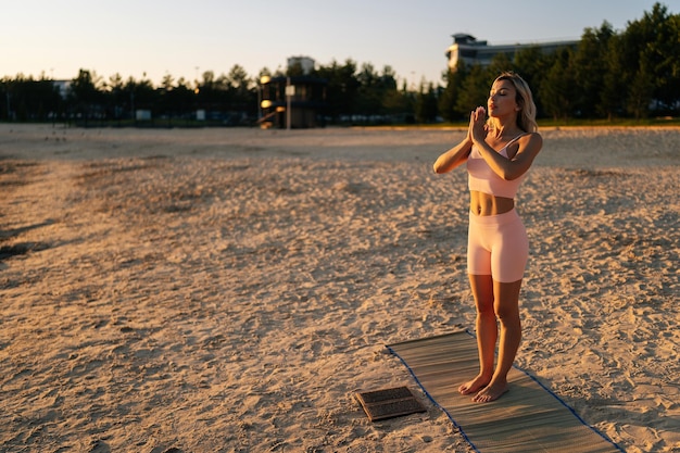 Mediteer een jonge vrouw die op een Sadhu-spijkerbord staat met gesloten ogen en een namaste-handteken maakt tijdens concentratiemeditatie op het zandstrand