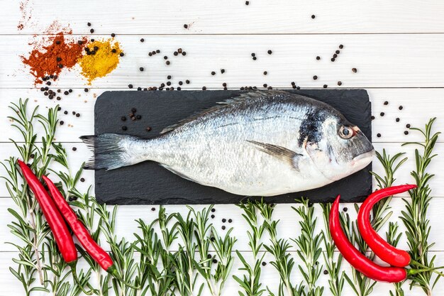 Mediterraan zeevruchtenconcept. Rauwe dorado vis met peper en rozemarijn op witte houten tafel. Kopiëren