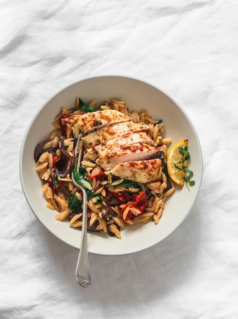 Mediterrane lunch orzo met champignons, gedroogde tomaten, spinazie en geroosterde kipfilet op een lichte achtergrond bovenaanzicht