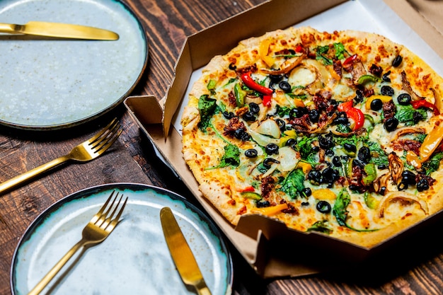 Средиземноморская пицца с оливками и сыром в картоне и в тарелках на столе