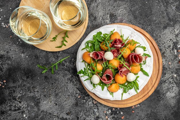 Mediterranean salad with prosciutto or jamon mozzarella and green basil leaves and Cantaloupe melon on white table traditional Spanish and Italian appetizer served with wholemeal grissini top view