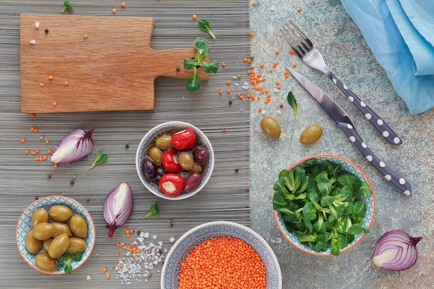 Mediterranean snacks set. Green and black olives, loaf of fresh multigrain bread, corn salad and red onion over old wood background. Top view with space for text. Flat lay.