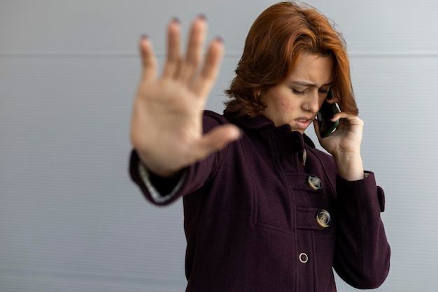 Medium closeup of a young Latin American woman 22 with red hair she doesn't want to be photographed while talking on her cell phone wearing a purple coat Focus on her face Concept Technology