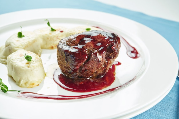 Medium rare filet mignon steak met bessensaus en aardappelgnocchi in een witte plaat op blauw tafelkleed