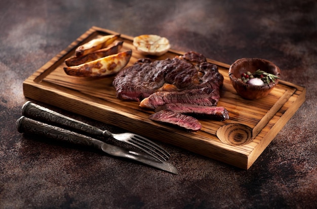 Medium rare grilled beef steak ribeye with fried potatoes on a brown rusty background