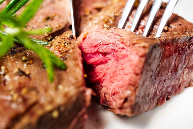 Medium rear beef steak. White plate with Piece of beef steak on fork.