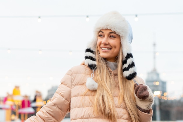 Medium shoot portret van romantische Europese dame draagt een lange stijlvolle winterjas en grappige pluizige hoed in besneeuwde dag Outdoor foto van geïnspireerde blonde vrouw genieten van winter stad