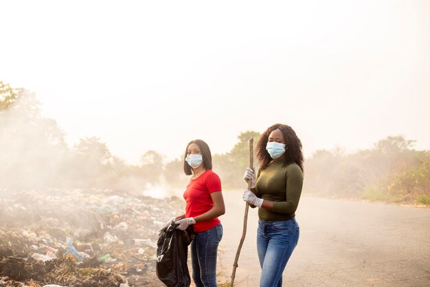 Medium shoot of two young black female sanitary worker wearing\
face mask whilst looking at camera