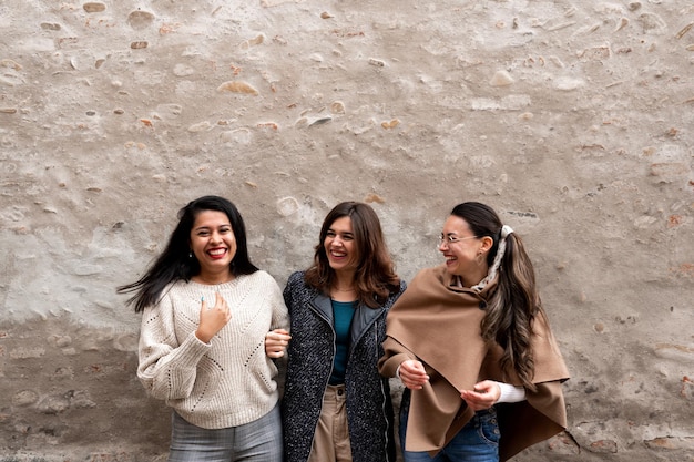 Medium shot drie gelukkige vrouwen tegen een oude stadsmuur die samen praten en plezier hebben.