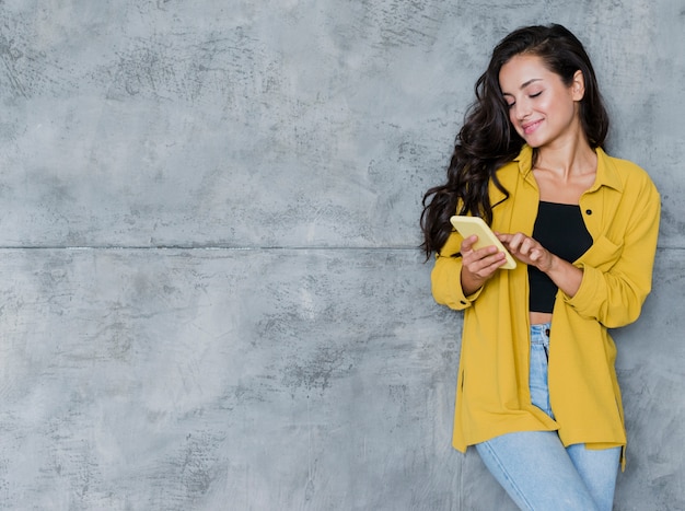 Ragazza del colpo medio con il fondo del cemento e del telefono