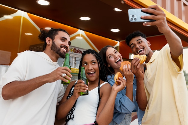 Foto amici felici del colpo medio che prendono selfie con il cibo