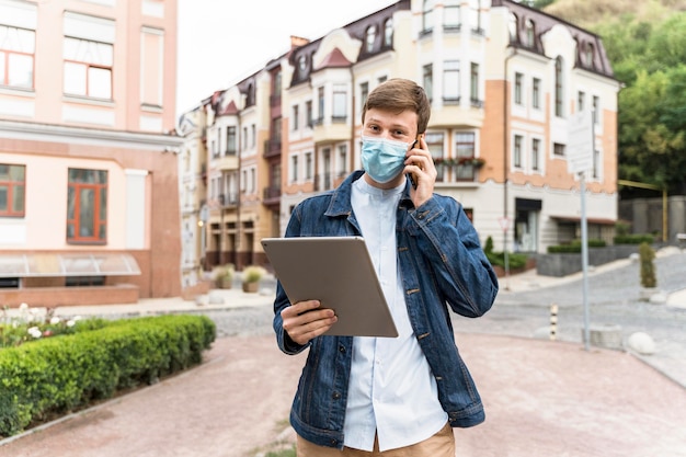 Medium shot man met een tablet terwijl hij een medisch masker draagt