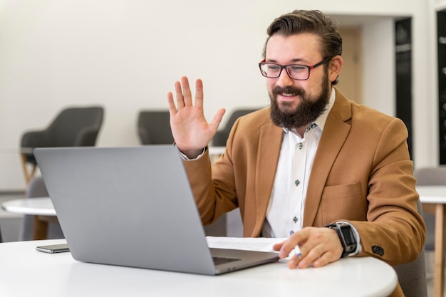 Medium shot man waving at laptop