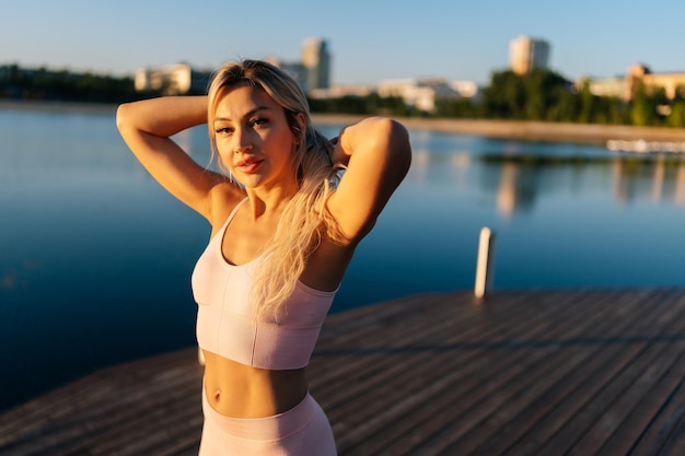 Medium shot portret van een vrij sportieve blonde vrouw in sportkleding die op een zonnige zomerochtend op een houten pier in het cite park staat