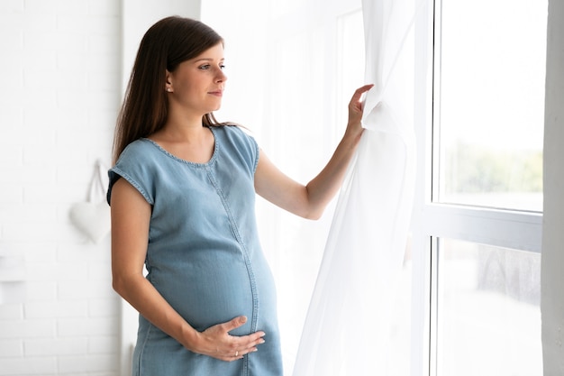 Medium shot pregnant woman looking on the window