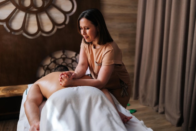 Medium shot van professionele vrouwelijke massagetherapeut met sterke handen die rug en schouders masseert van een gespierde man die op een massagetafel ligt Sportieve man die een ontspannende massage krijgt in een spa-salon