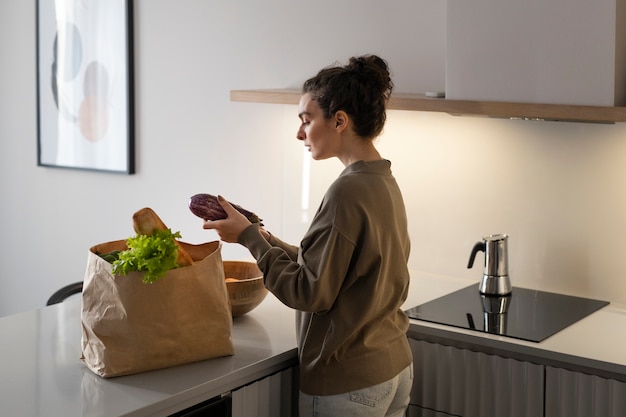 Foto donna del colpo medio con generi alimentari a casa