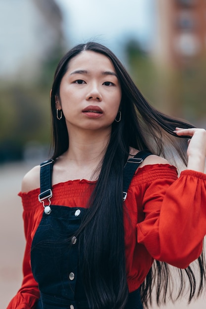 Medium shot of a young asian girl in red sweater touches her hair while looking at the camera