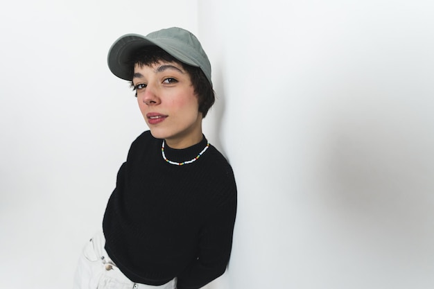 Photo medium shot of a young croppedhair woman weaing black jumper and a cap looking at the camera with