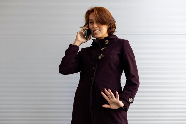 Medium shot of young Latin American woman 22 red hair listening to a voice message making a gesture with her outstretched palm and fingers wearing a purple coat Concept Technology