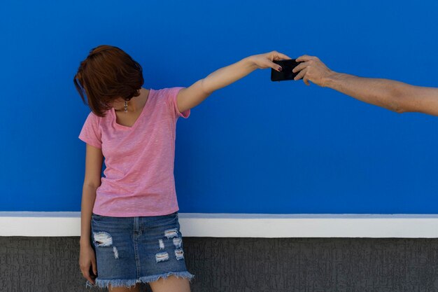 Photo medium shot of young woman 22 with latin american red hair sadly detaching herself from her cell phone from which she does not want to part blue wall background portrait concept