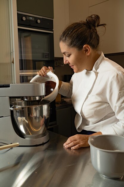 Mediumadult woman pastry chef adding chocolate in planetary\
mixer owner of her own business