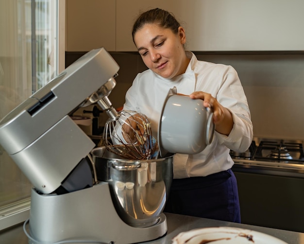 プラネタリー ミキサーで小麦粉を追加するミディアムアダルトの女性パティシエが自分のビジネスの所有者