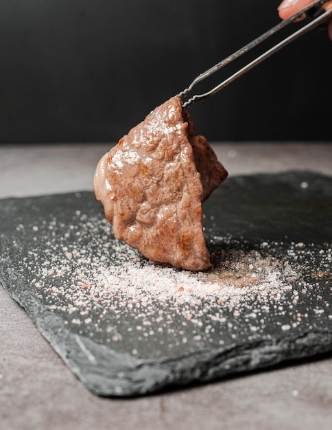 A mediumrare piece of high marble Sirloin A5 Wagyu picked with BBQ tongs and dip in Himalayan salt on a black stone plate Served for Yakiniku